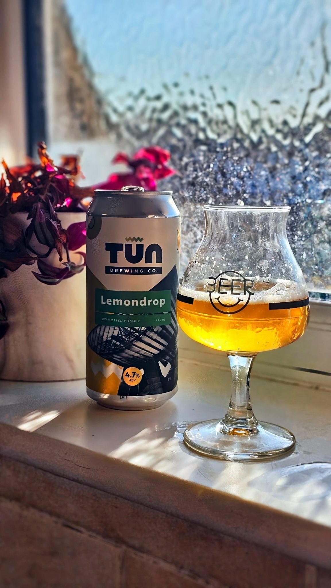 A Lemondrop can beside a glass of golden Pilsner in sunlight